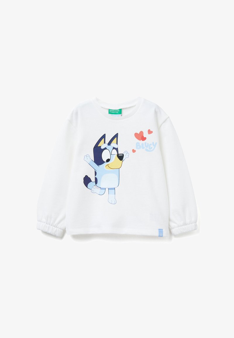 Una camicia bianca a maniche lunghe con un personaggio di cartone animato di un cane con pelo blu, un muso giallo e cuori rossi. Il tessuto ha una consistenza morbida.