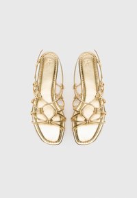 Gold metallic sandals with a flat sole, featuring intricate crisscross straps and knot detailing. Smooth texture with a square toe design.