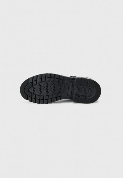 Black rubber shoe sole with a textured surface, featuring deep treads and a logo. Shaped for traction and durability.