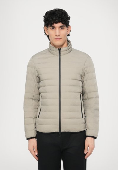 Veste matelassée gris clair avec un col montant, une texture matelassée horizontale, une fermeture éclair frontale et des poches latérales. Accents noirs sur la fermeture éclair et les poignets.