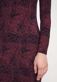Vestido de manga larga en burdeos oscuro y negro con patrones florales y de hojas. Tejido texturizado con una silueta ajustada.