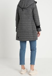 Grijze pufferjas met een capuchon, voorzien van een gestructureerd patroon, zwarte manchetten en een halflange snit, gecombineerd met blauwe jeans en lichte schoenen.