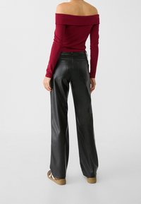 Bordový svetr bez ramínek s dlouhými rukávy, kombinovaný s širokými kalhotami z černé umělé kůže. Mezi výrazné detaily patří kapsy a hladký povrch.