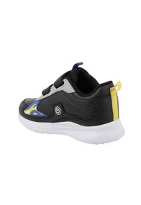 Scarpa sportiva bianca e nera con dettagli gialli e blu, chiusure a velcro, suola bianca e linguetta gialla sul tallone.