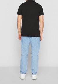 Svart kortärmad polo skjorta, matchad med ljusblå denimjeans. Jeansen har en avslappnad passform och bärs med vita sneakers.