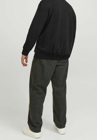 Felpa nera con bordo elastico, abbinata a jeans grigi antracite a vestibilità ampia. Sneakers bianche completano il look, viste da dietro.