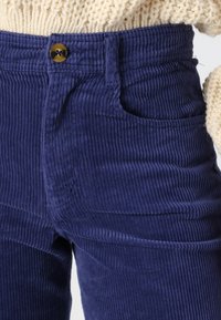 Námornícke kordové nohavice so širokými rebrami, s prednou kapsou a hnedým gombíkom na zapínanie v oblasti pásu. Mäkko textúrované a štruktúrovaný strih.