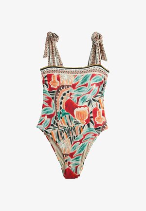 Vienos dalies maudymosi kostiumėlis su spalvingais abstrakčiais botaniniais ir vazos raštais, petnešėlėmis, kurios susiriša ant pečių, ir užrašu „vacances à la plage“ palei viršutinį kraštą.