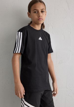 Zwarte katoenen t-shirt met wit Adidas-logo en gestreepte mouwen. Voorzien van een klassieke ronde hals en een ontspannen pasvorm. Achtergrond met een gestructureerde muur.