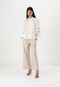 White blouse with lace detailing, pleated front, and puff sleeves, paired with beige wide-leg trousers and purple heeled sandals.