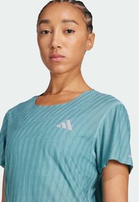 T-shirt de sport en bleu clair avec un motif texturé, col rond et manches courtes. Comprend un logo contrastant sur la poitrine.
