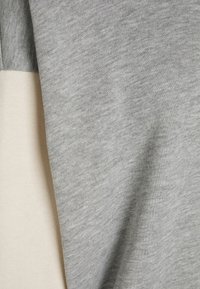 Primo piano di un morbido tessuto lavorato a maglia in grigio chiaro e bianco sporco con una texture sottile e pieghe drappeggiate.