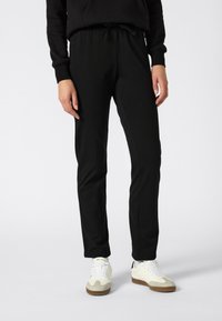 Black athletic pants made of soft fabric, featuring a drawstring waist, tapered fit, and side seam details. Worn with white sneakers.