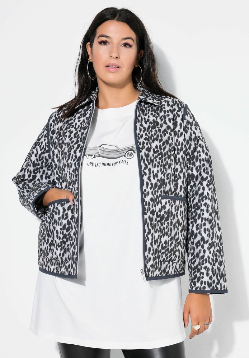 Leopardprint jakke med lynlås foran, grå accenter og to sidelommer, båret over en hvid grafisk t-shirt. Blødt, struktureret stof.