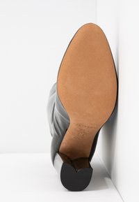 Chaussure en cuir noir à bout pointu, présentant une surface lisse et un talon légèrement surélevé et incurvé. La semelle inférieure est de couleur beige clair.