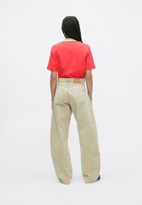 Raudona trumpomis rankovėmis marškinėliai, derinami su laisvai krentančiomis kreminėmis kelnėmis. Kelnėse matomas diržo etiketės ženklas ir subtili tekstūra. Paprastas ir neutralaus dizaino.