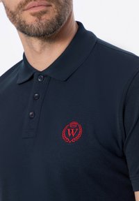 Námořnické polo tričko vyrobené z texturované látky, s tříknoflíkovým zapínáním a červeným vyšitým logem s vavřínovým designem na levé hrudi.