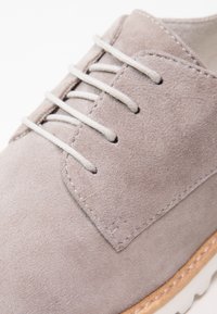 Scarpa in suede grigio chiaro con una texture liscia, dotata di lacci grigi e una suola in gomma beige. Punta rotonda e dettagli di cucitura discreti.