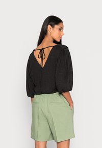 Top preto texturizado com costas em V e detalhe de laço, combinado com calções verdes claros de corte descontraído, com bolsos laterais e um tecido leve.