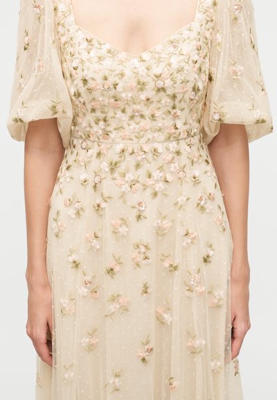 Robe beige clair avec manches bouffantes, présentant de délicats motifs floraux brodés roses et blancs ainsi que de subtils détails de feuilles.