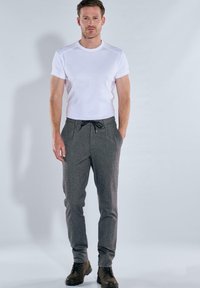 Männliches Outfit mit einem taillierten weißen Kurzarm-T-Shirt und grauen gemusterten Hosen mit Kordelzug, kombiniert mit dunklen Stiefeln.