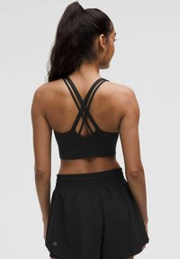 Zwarte sportbeha met gekruiste banden, gecombineerd met zwarte shorts. De stof lijkt glad, lichtgewicht en rekbaar met een elastische tailleband.