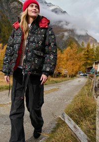 Czarna kwiatowa kurtka puchowa z czerwonymi akcentami, o luźnym kroju; zestawiona z szerokimi czarnymi spodniami. Noszona z czerwonym dzianinowym kapeluszem. W tle widoczne góry.
