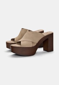 Beige ruskind slide-on sko med en bred forstribe, sat på en struktureret brun træplattformhæl på cirka 10 cm høj.