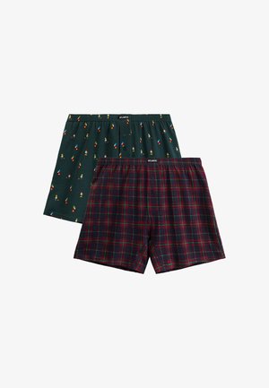 Dwie pary męskich bokserek, jedna ciemnozielona z kolorowym wzorem krasnali, druga granatowa w czerwoną i zieloną kratę, obie z rozporkiem na guziki i elastycznym pasem.