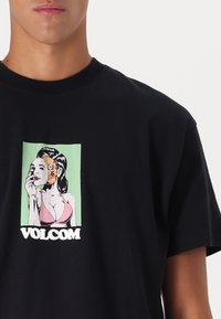 Zwarte katoenen T-shirt met een grafische afdruk van een illustratie van een vrouw, accentueert in groene en roze tinten, en "VOLCOM" tekst.