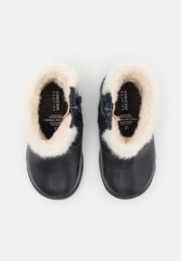 Cizme negre din piele la gleznă, cu căptușeală pufoasă de culoare crem, sistem de închidere cu fermoar pe lateral și bot rotund. Textura din piele cu izolație interioară moale.