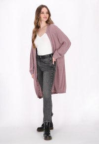 Cárdigan largo de frente abierto en suave y texturizado morado claro, combinado con una blusa blanca, jeans negros de tiro alto y botas negras con cordones.