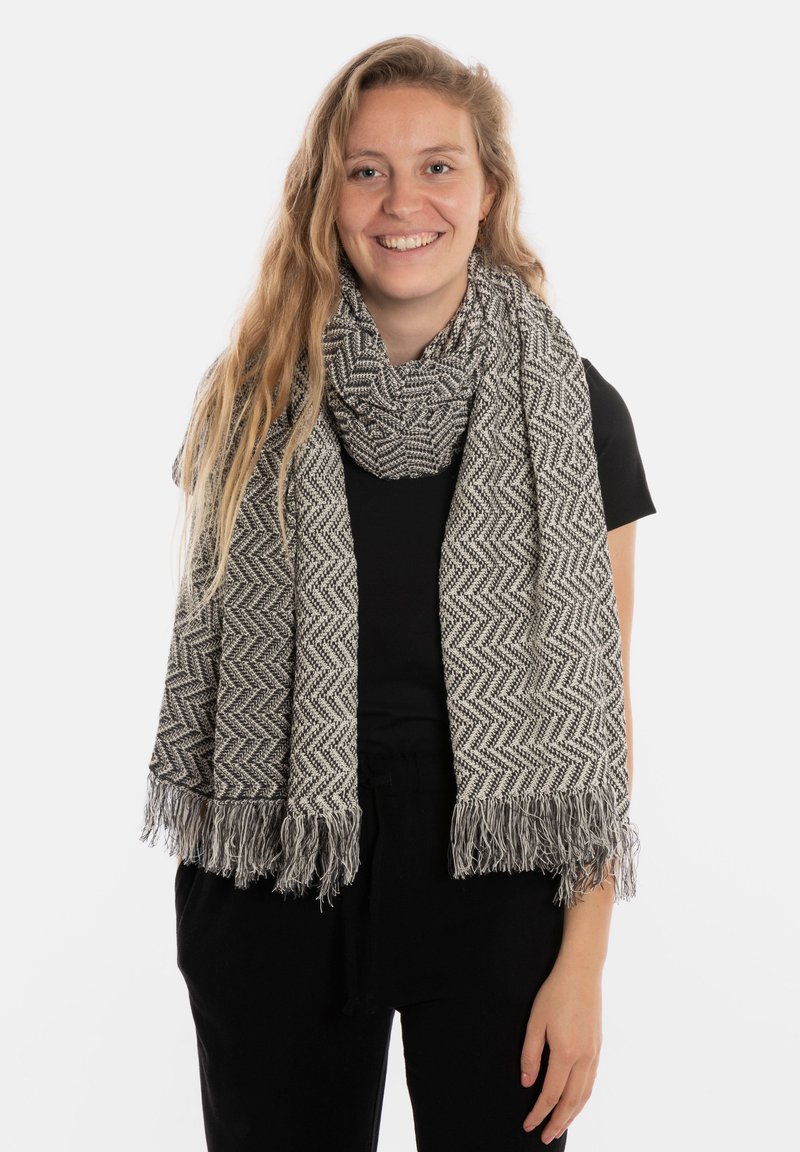 Écharpe à motif chevron gris et blanc avec des extrémités frangées, fabriquée en tissu texturé, enroulée autour du cou.