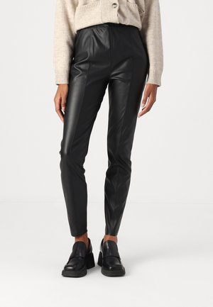 Pantaloni neri in ecopelle con un design elegante, vita alta e dettagli decorativi lungo i lati; abbinati a mocassini neri spessi.