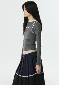 Graues Langarmshirt mit weißem Saum, kombiniert mit einem marineblauen Faltenrock, der einen Spitzenrand und ein rotes Gewebemuster am Bund hat.