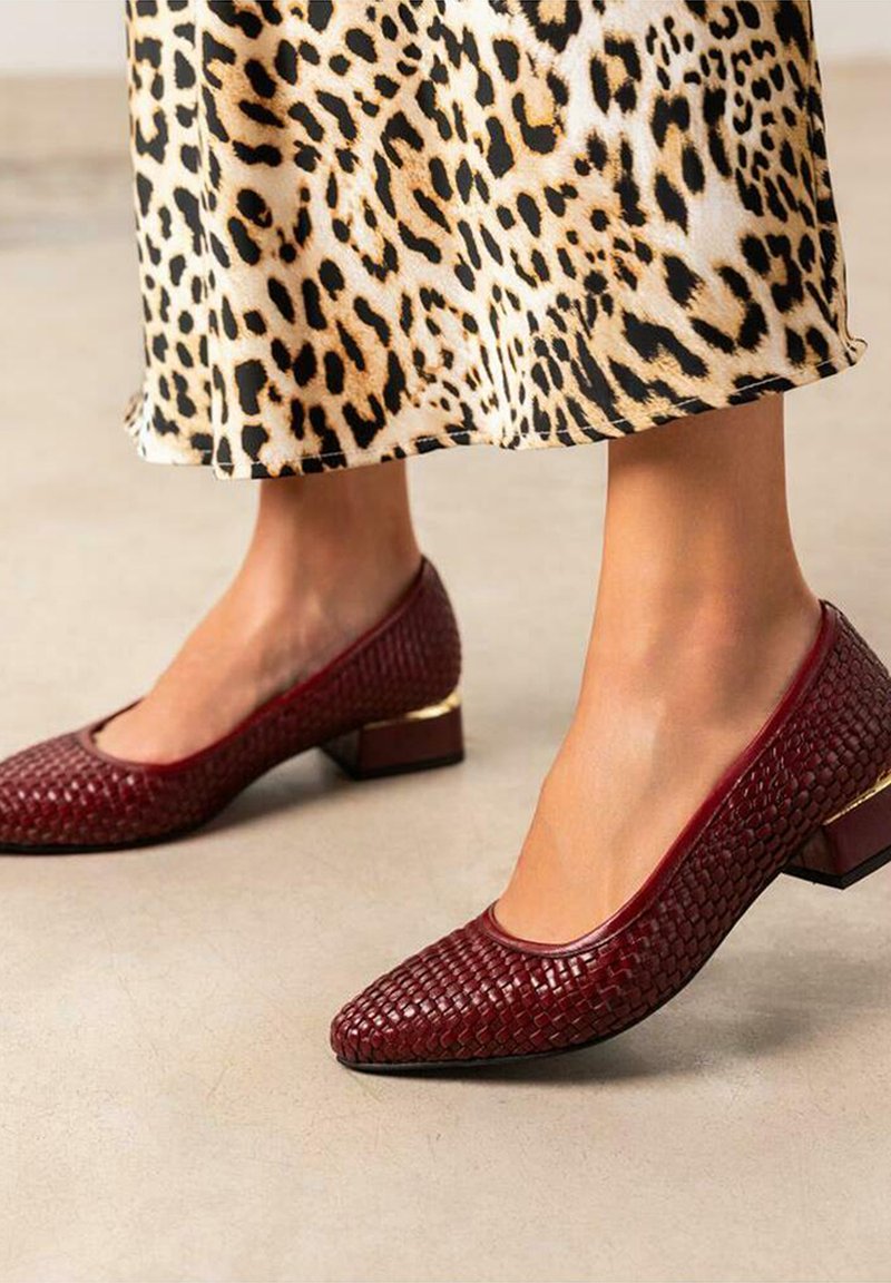 Zapatos de tacón bloque trenzados de cuero en color burdeos con puntera redonda y un acento dorado en el tacón, combinados con una falda de estampado de leopardo.