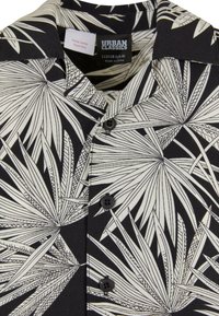 Juodas trumpas rankovėmis marškinėliai su balta lapų raštu, turintys apykaklę, penkis mygtukus ir priežiūros etiketę. Pagaminti iš lengvos medžiagos.