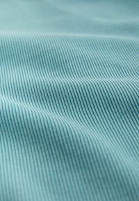 Lähikuva vaaleansinisestä ribbineuloksesta, jossa näkyy koholla olevat rinnakkaiset linjat ja pehmeät laskokset, korostaen tekstuuria ja materiaalin yksityiskohtia.