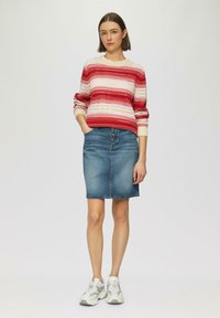 Rood, roze en crèmekleurige gestreepte gebreide trui met een geribbelde halslijn, gecombineerd met een blauwe denim kokerrok en lichtgrijze sneakers.