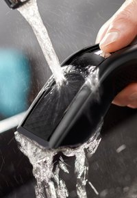 Water stroomt over een zwarte elektrische scheerapparaat met een getextureerd oppervlak, vastgehouden door een hand, wat het waterdichte ontwerp en de slanke vorm benadrukt.