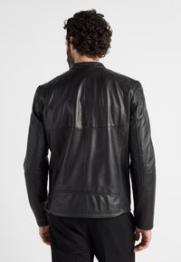 Zwarte leren jas met een gladde textuur, voorzien van gewatteerde schouderaccenten, een getailleerd ontwerp en subtiele stikdetails op de achterkant.