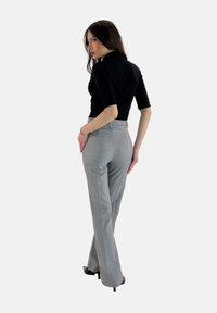 Pantalons gris sur mesure à taille haute, avec des poches sur les côtés et une texture lisse, associés à un haut noir ajusté, vus de dos.