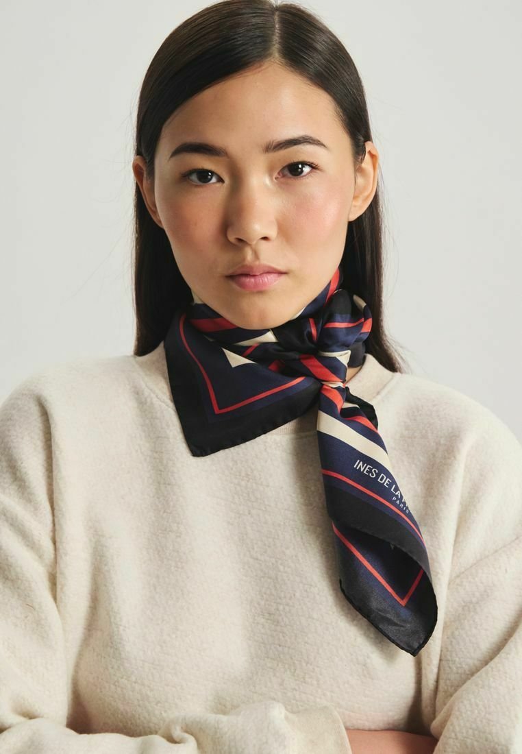 Foulard en soie avec une base marine et des motifs géométriques rouges et crème, noué autour du cou, associé à un pull crémeux texturé.