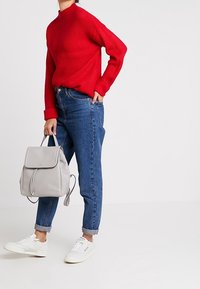 Röd ribbad tröja med hög krage, kombinerad med blå jeans med uppvikt byxben, grå ryggsäck och vita sneakers. Modern och avslappnad stil.