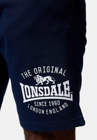 Marineblauwe shorts van katoen met witte bedrukte logo-details, voorzien van een leeuwengrafiek en tekst: "DE ORIGINELE LONSDALE SINDS 1960 LONDEN ENGELAND."