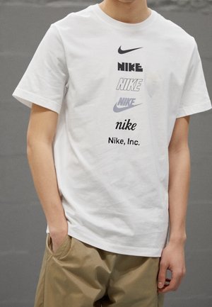White cotton t-shirt featuring multiple Nike logos in varying sizes and styles, with a relaxed fit and short sleeves.