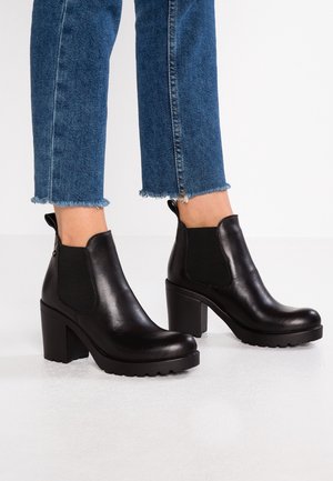Sorte læderankelstøvler med høj blokhæl, elastiske sidepaneler og en let chunky sål. Tekstureret finish og minimalistisk design.