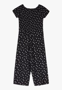 Combinaison noire avec un corsage froncé, des manches courtes et des pois blancs. Le design à jambes larges a une texture fluide.