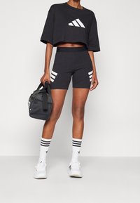 Černé zkrácené tričko s bílým logem, černé přiléhavé šortky s bílými pruhy, černá taška, bílé ponožky se třemi černými pruhy, bílé tenisky.