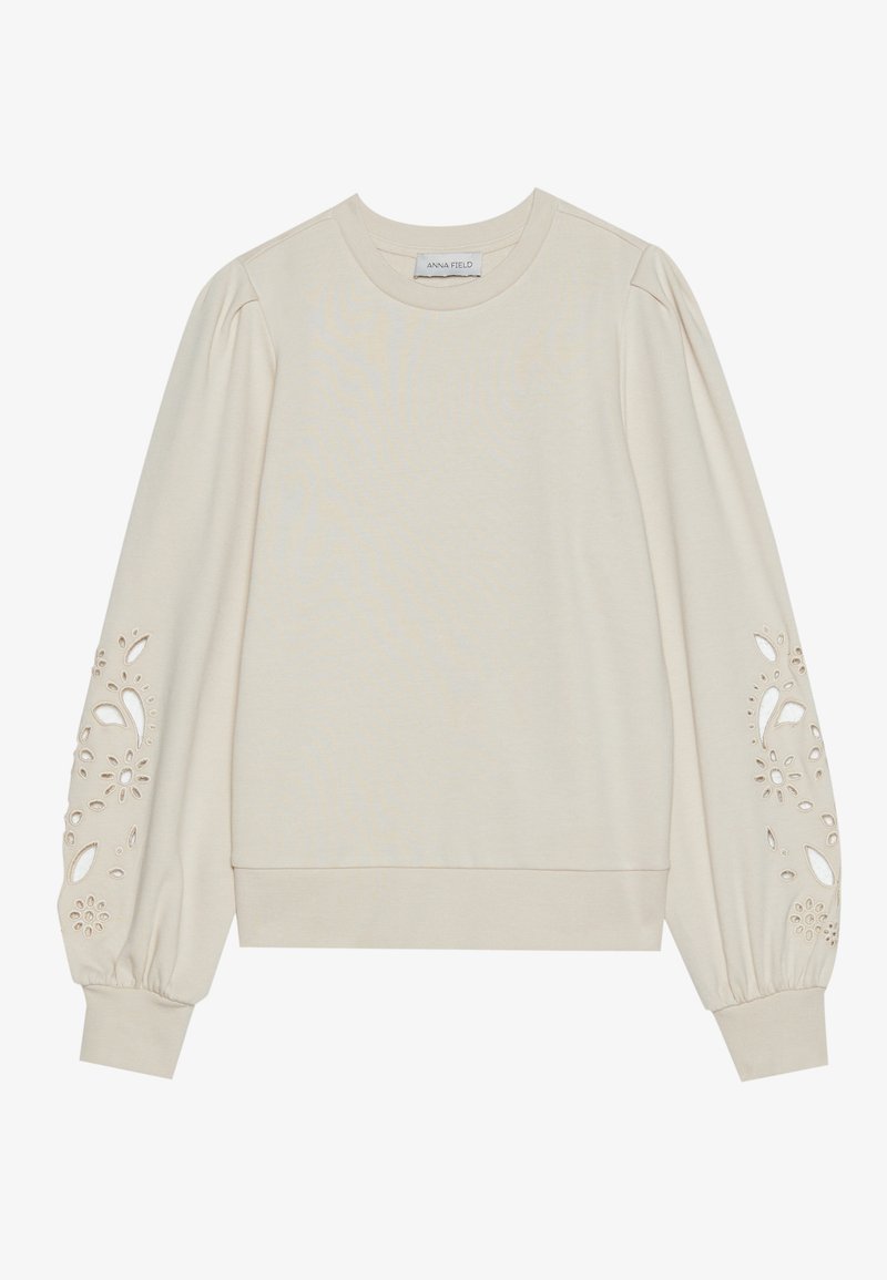 Maglione beige chiaro con maniche ampie e motivi floreali ritagliati sui polsini. Tessuto morbido e orlo a coste per un aspetto aderente.